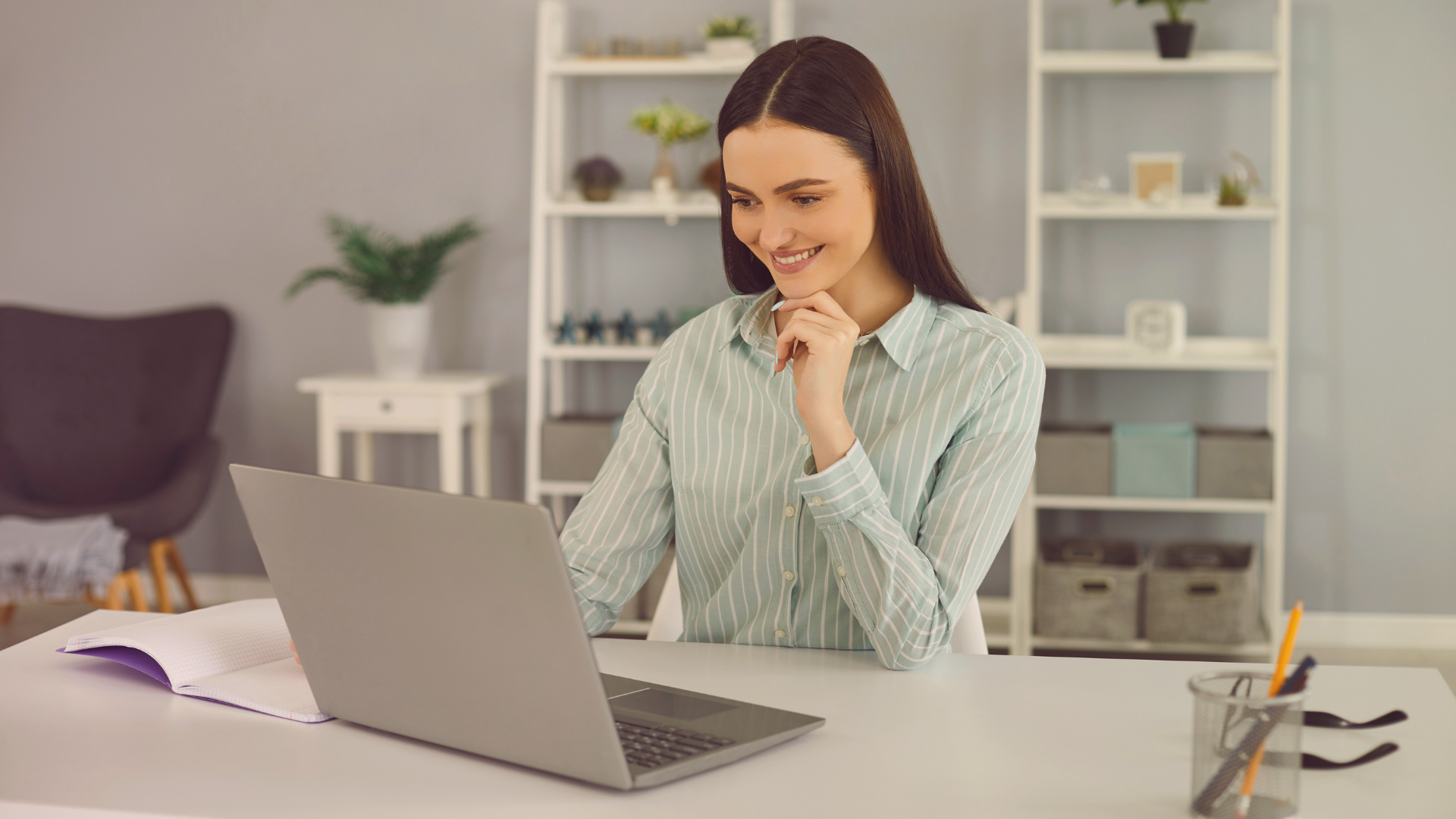 Eine Frau sitzt an ihrem Schreibtisch und blickt erfreut in den Computer-Bildschirm